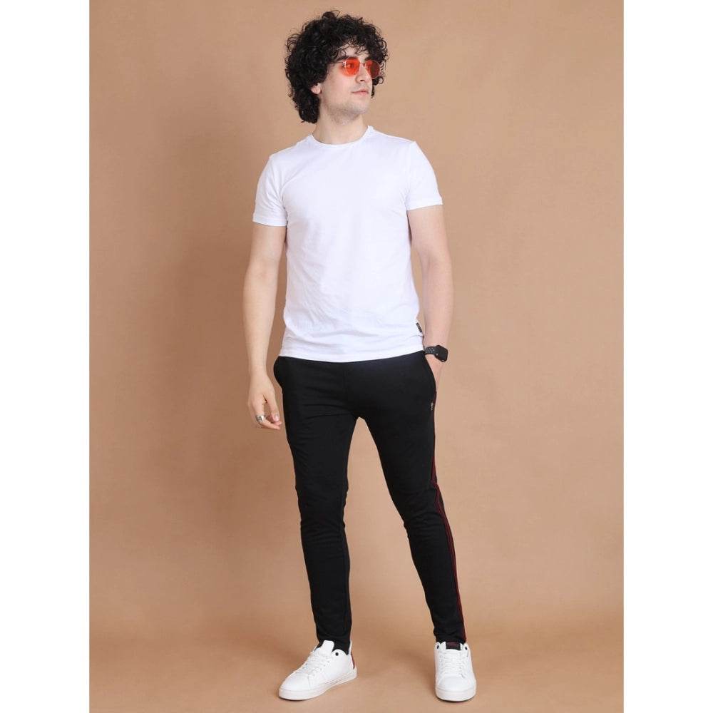 Man wearing a white t-shirt, black pants, and white sneakers against a brown background