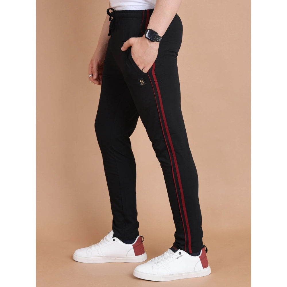 Person wearing black pants with red stripes and white sneakers on a beige background